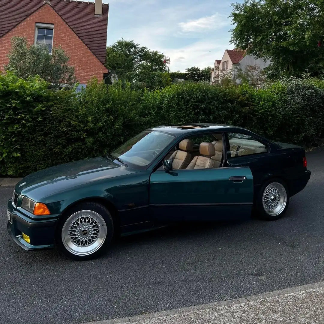 Coupé BMW Série 3 des années 1980 en vert foncé avec intérieur en cuir beige et jantes en alliage argentées.